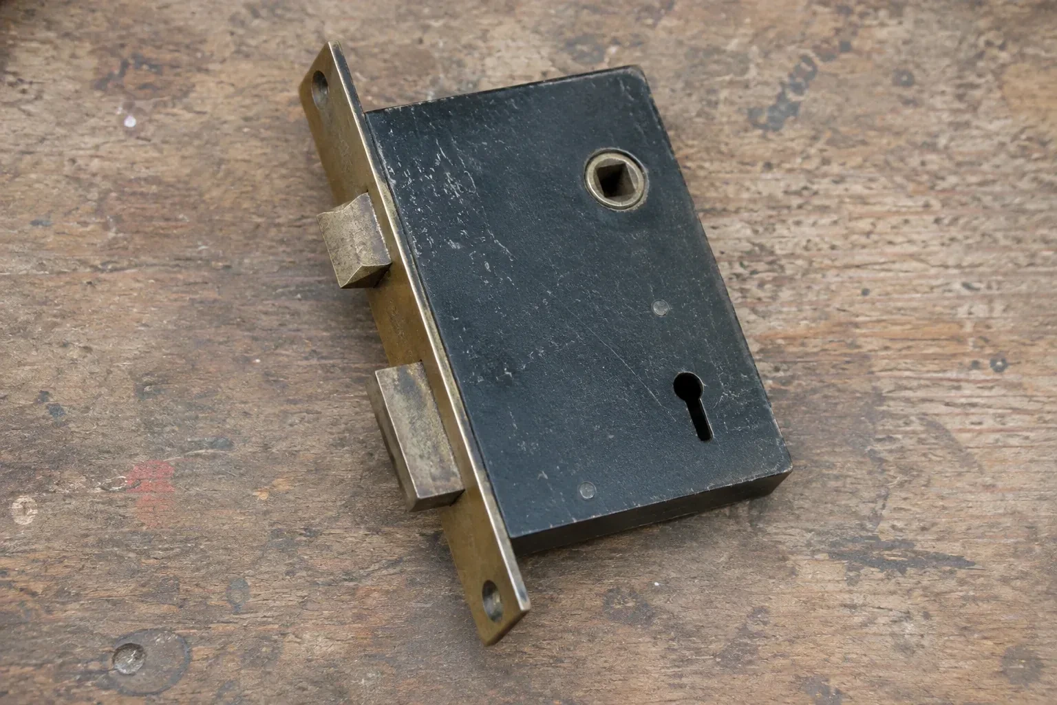 Closed mortise lock case with spindle opening, keyhole, latch and deadbolt on a wooden workbench. — Vintage Mortise Lock Service, Scugog