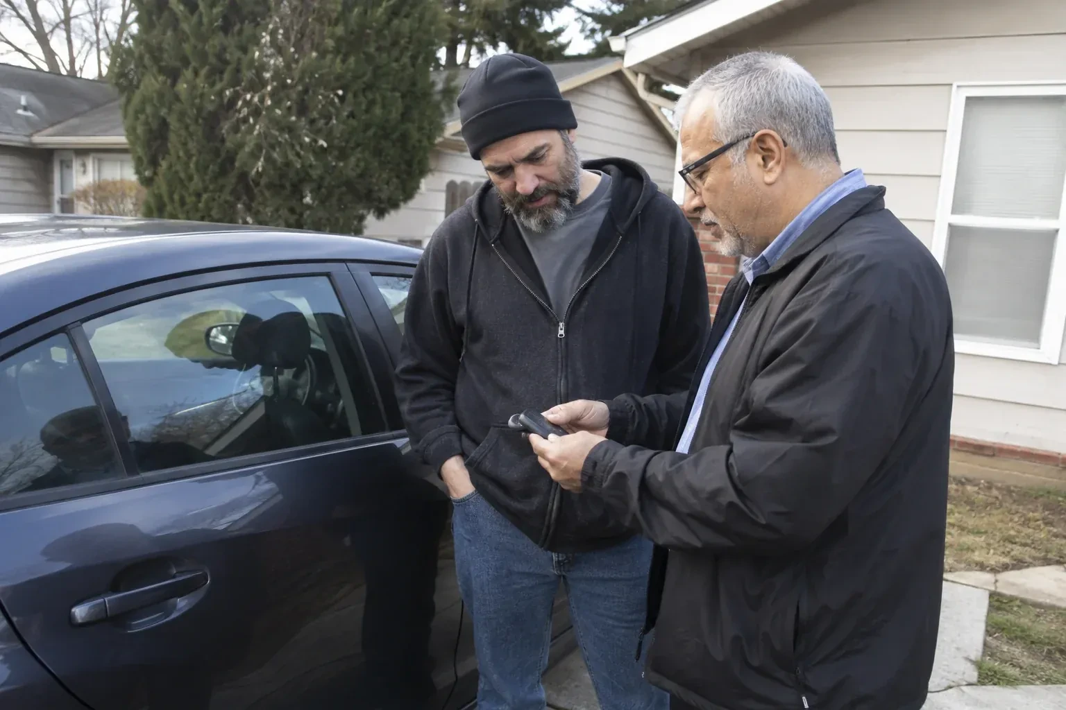 Two adults discussing a key fob beside a parked car. — Car Lockout Service, Scugog